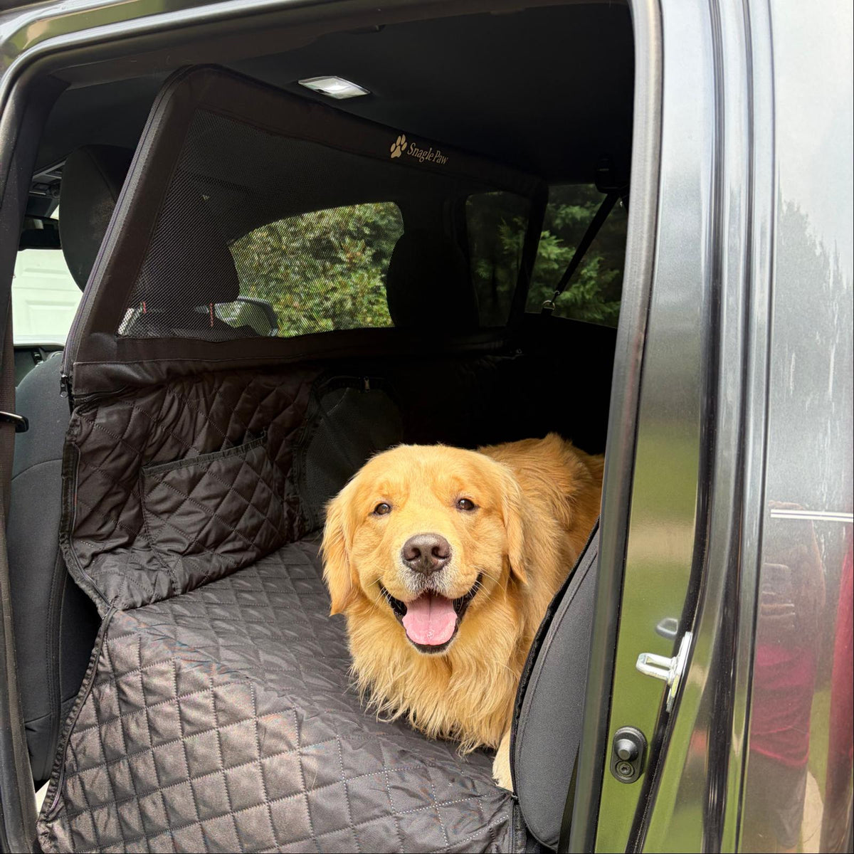 A Golden Retriever lying comfortably on a black Snagle Paw dog car seat cover with hard bottom extension and patented ultra-high mesh barrier in the back seat.