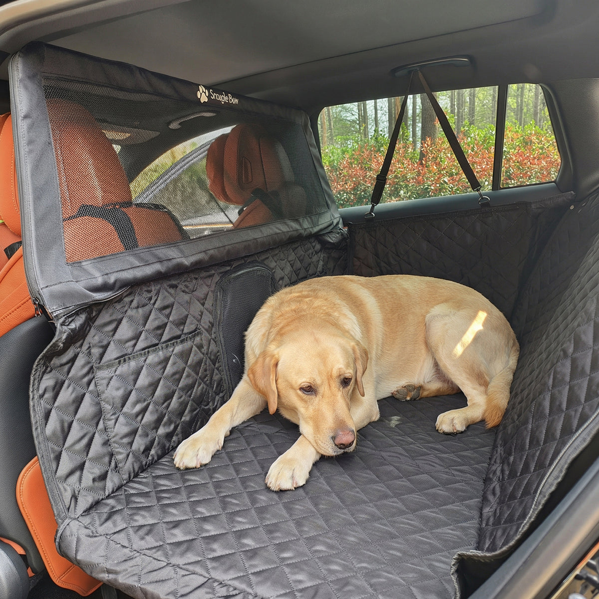 A yellow Labrador Retriever lying comfortably on a black hard-bottom Snagle Paw dog car seat cover with an ultra-high mesh barrier.